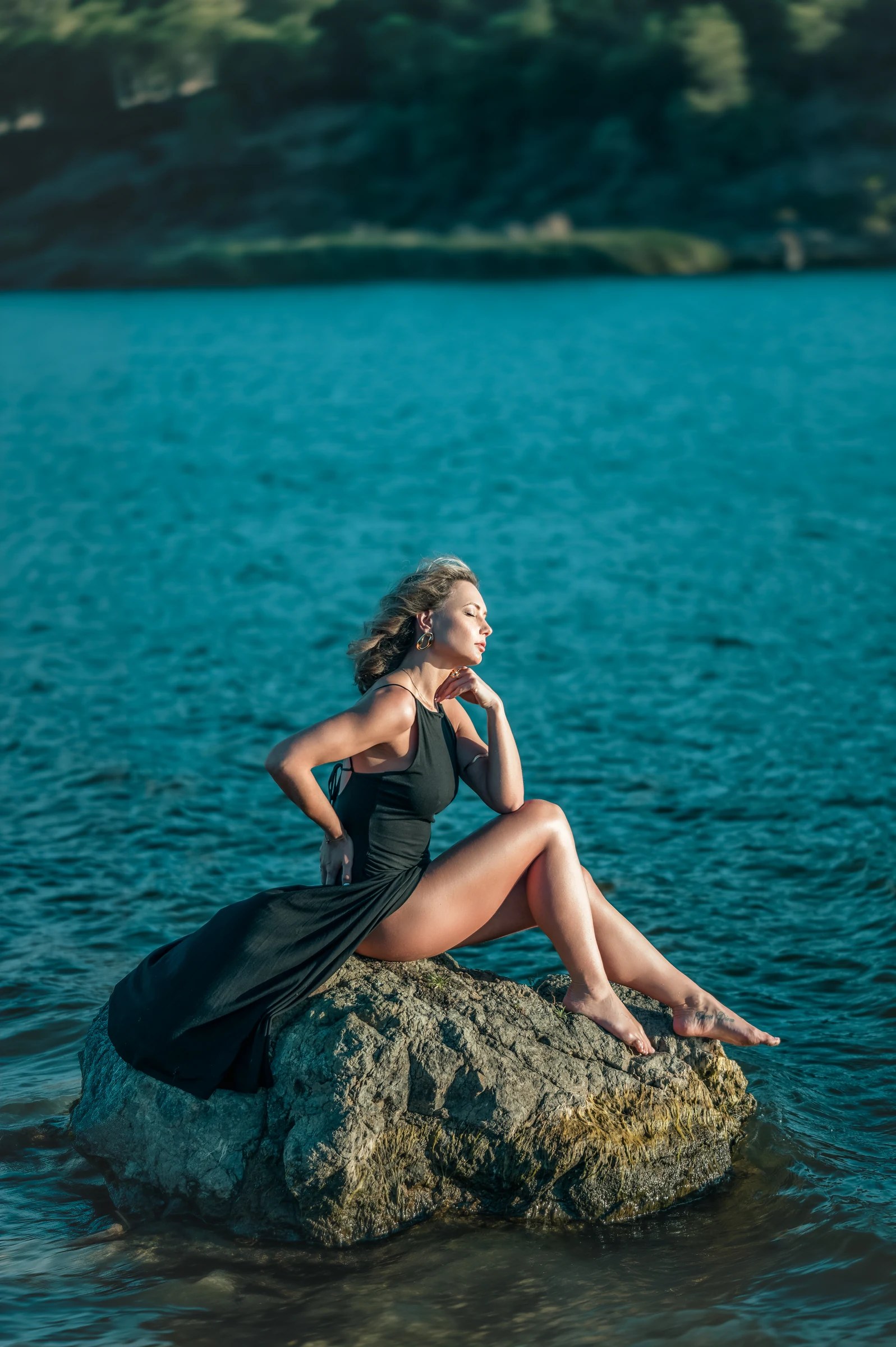 Olesia Prodan seated on a coastal rock in a flowing dark dress