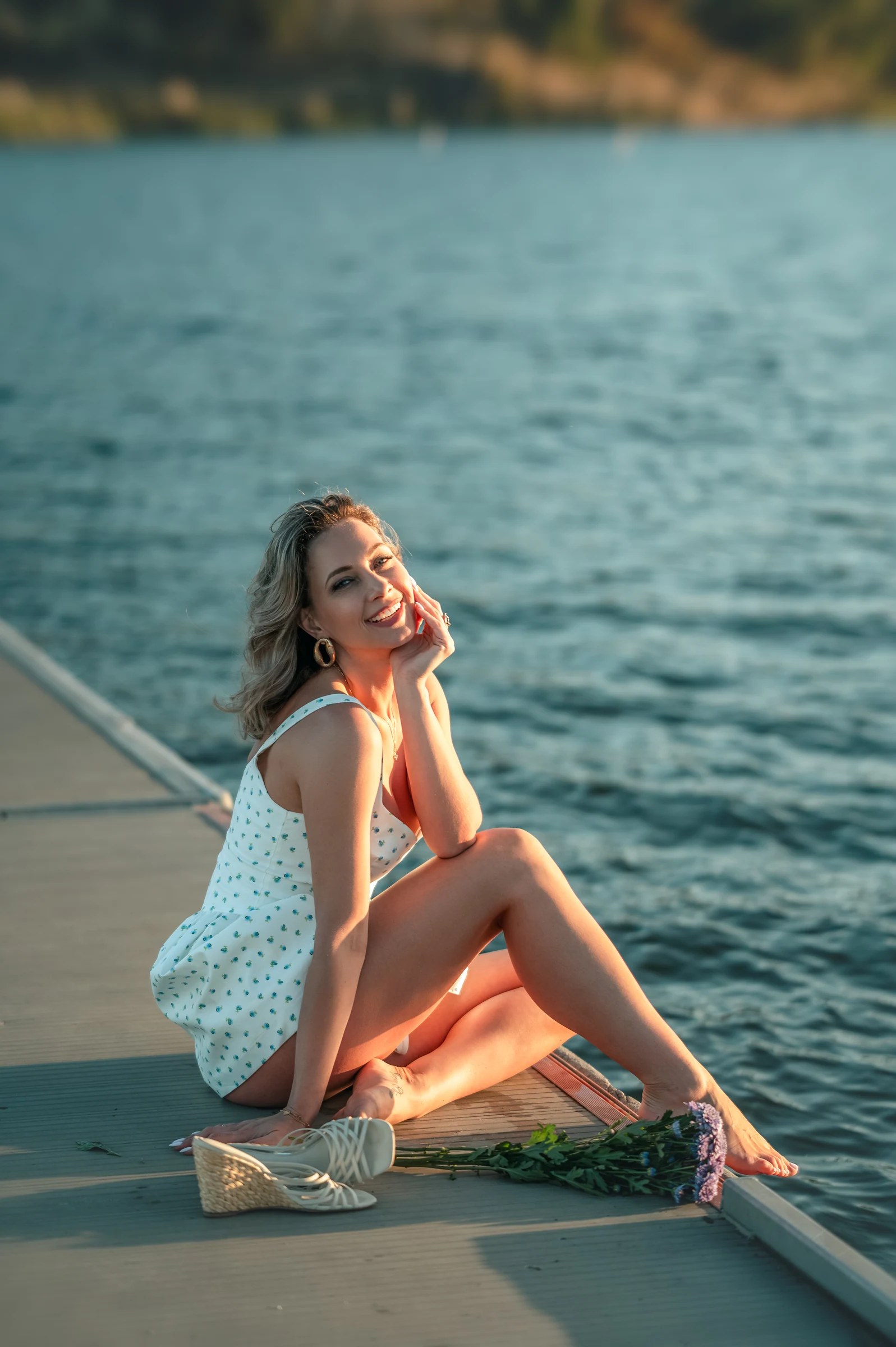 Olesia Prodan smiling in a white summer dress beside the water